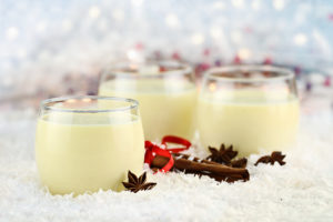 Three glasses of fresh eggnog with cinnamon sticks and star of anise ready for the Christmas season with copy space. Extreme shallow depth of field.